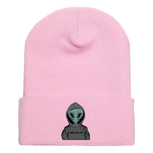 Pink acrylic beanie featuring a serious cartoon alien in a gray hoodie with the word “BELIEVE” printed across the front.