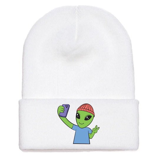 White acrylic beanie featuring a cartoon alien in a red beanie taking a selfie and flashing a peace sign with one hand.